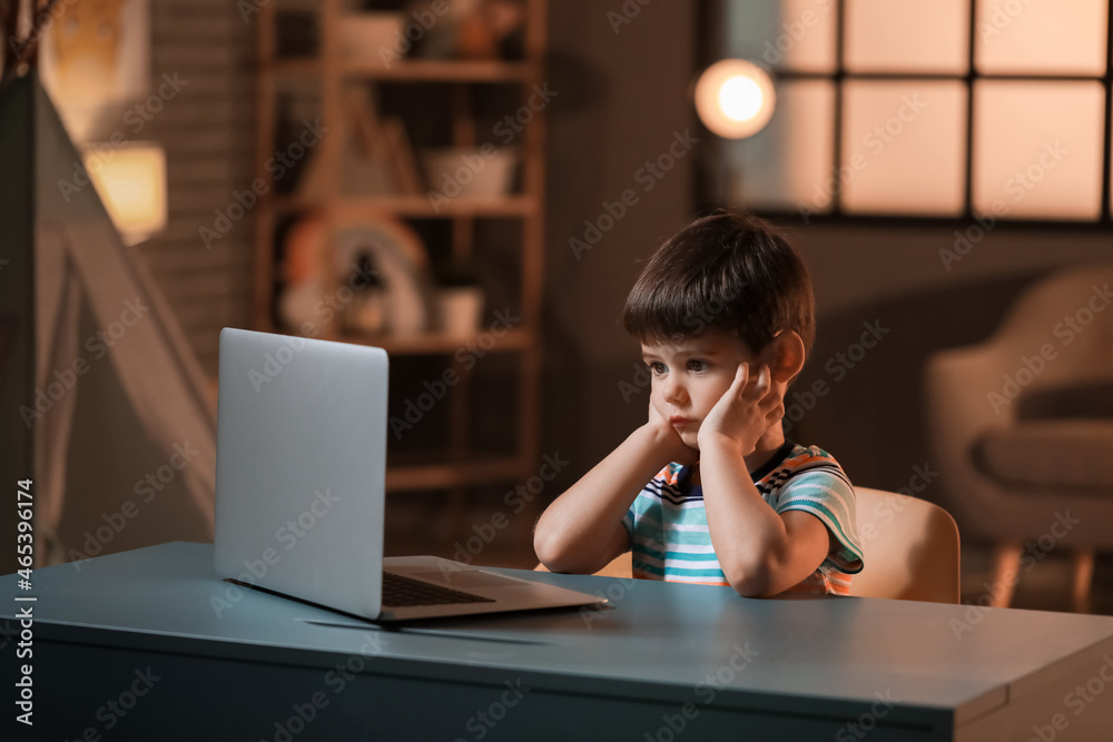 Little boy watching cartoons on laptop at table late in evening
