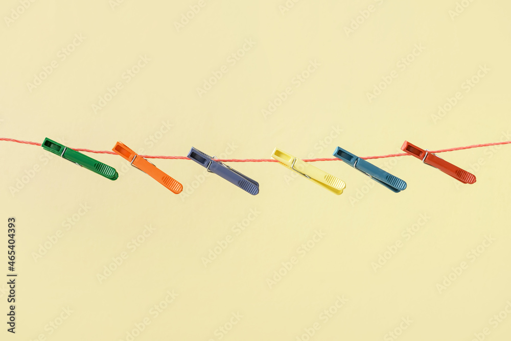 Different clothespins hanging on laundry line against color background