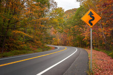 Winding Road Signpost With Fall Foliage On Highway