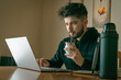 young man working / studying in front of a laptop while drinking a mate (Argentine drink)