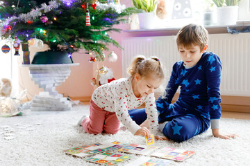 Two little chilren, cute toddler girl and school kid boy playing together card game by decorated Christmas tree. Happy healthy siblings, brother and sister having fun together. Family celebrating xmas