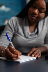 Poster - Close up of worker taking notes with pen on notebook at desk. Young adult writing information on textbook files while working from home on business project. Woman with remote work
