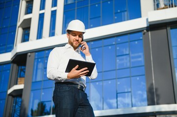 Portrait of man engineer at building site. Male construction manager wearing white helmet and yellow safety vest