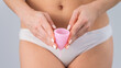 Close-up of a woman in white cotton panties holding a pink menstrual cup against a white background. Alternative to tampons and pads