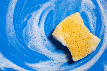 cleaning sponge wiping foam soap suds on blue background, household washing concept