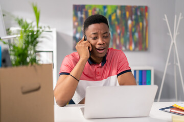 Wall Mural - A customer service employee is sitting in an office at desk in front of laptop screen, talking on phone, trying to solve caller's problem checking available dates taking complaints, his face disgusted