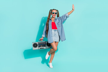 Sticker - Photo of beautiful friendly young lady wear jeans shirt dark eyewear smiling holding boombox waving arm hi isolated turquoise color background