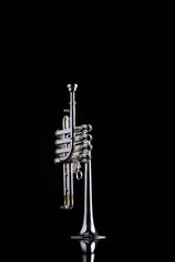 A four valve piston silver plated piccolo trumpet on a black reflective surface. A brass instrument common to baroque music.