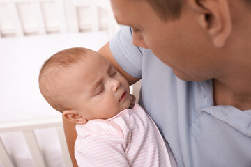 Happy father with his cute sleeping baby near crib indoors, closeup