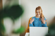 © Strelciuc - Front view of a woman actively participating in an online interview sitting on an armchair. Red hair and freckled face. Video conversation.