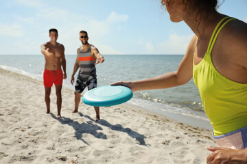 Canvas Print - Friends playing with flying disk at beach on sunny day