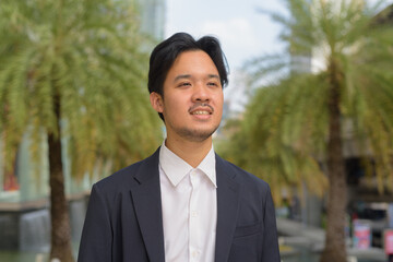 Canvas Print - Portrait of happy Asian businessman thinking outdoors in the city