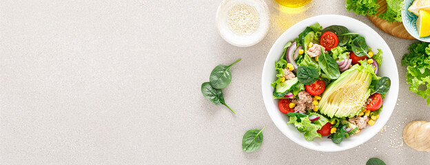 Wall Mural - Avocado and tuna fresh vegetable salad with tomato, cucumber corn, onion, lettuce and spinach. Healthy and detox food concept. Ketogenic diet. Buddha bowl dish on light background. Top view. Banner.