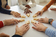 © Studio Romantic - Group of multiethnic business people and teammates sitting around office table put little wooden human figures in circle as symbol of community, team, help, cooperation, collaboration and teamwork