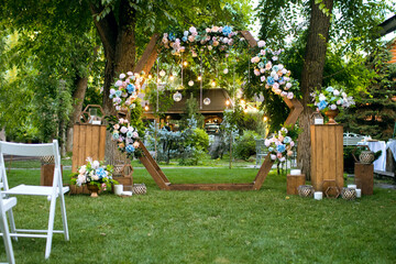 Wooden arch for the wedding ceremony and chairs. The wedding arch is decorated with bright flowers and lights in the form of a garland with candles. Beautiful decoration of the wedding ceremony