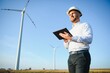 © Serhii - Young engineer man looking and checking wind turbines at field