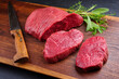 Raw dry aged bison beef rump steak piece and slices offered with herbs as close-up on wooden design board