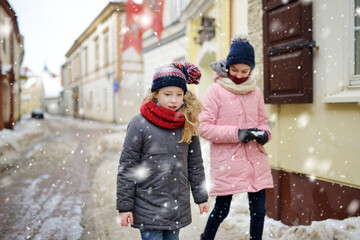 Wall Mural - Two adorable young sisters having fun on beautiful winter day in a city. Cute children having a walk in winter town.