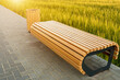 Modern comfortable wooden bench without a back and garbage can made of wooden slats on paving slabs in a park