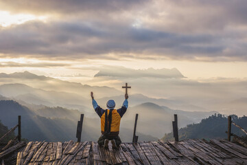 Humans pray to GOD while holding a crucifix symbol with a bright sunbeam on the mountain at sunset or sunrise time. Christian, Christianity, Religion copy space background.