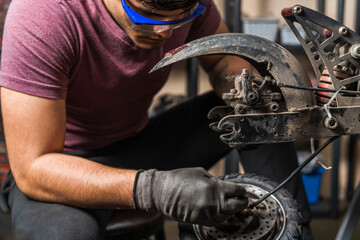 A seated mechanic removes the wheel of an electric scooter for inspection