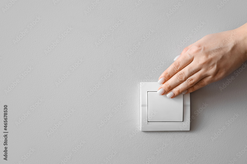 Woman switching on light near light wall, closeup