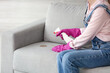 Woman in gloves cleaning dirty stain on sofa at home
