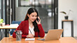 © Prathankarnpap - Smiling businesswoman checking information on laptop computer and talking on mobile phone.