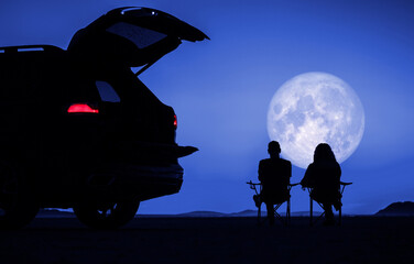 couple seating next to their vehicle and enjoying full moon vista