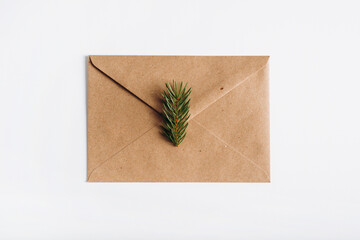 Greeting envelope for Christmas or Happy New Year on white table, top view. Closed gift craft envelope for holiday with sprig of pine, flat lay. Festive letter with wishes or congratulations concept