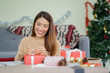 © chinnarach - close up young asian woman try to put ribbon on wrapped gift box at living room with pine tree decoration for merry Christmas and happy new year festival season concept