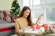 © chinnarach - close up young asian woman try to put ribbon on wrapped gift box at living room with pine tree decoration for merry Christmas and happy new year festival season concept