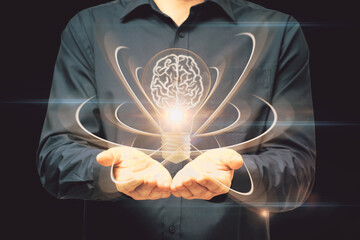 Poster - Close up of male hand holding abstract light bulb on dark wide background with digital brain and atom outline. Artificial intelligence, science and innovation concept.