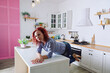 © Oleksandra - woman cooking in kitchen. Young redhead curly woman 30+ in blue jeans and a shirt sitting and relaxing in her bright clean kitchen. Healthy happy lifestyle. Leisure. Housewife.