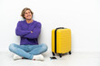 © luismolinero - Young blonde man with suitcase sitting on the floor with arms crossed and happy