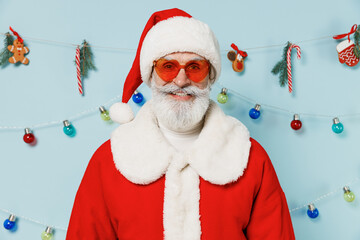 Old bearded Santa Claus man 50s wear Christmas hat red suit clothes glasses look camera posing isolated on plain blue background studio. Happy New Year 2022 celebration merry ho x-mas holiday concept