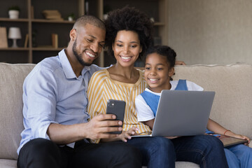 Wall Mural - Addicted to modern tech happy bonding african american family parents and small kid daughter posing for photo on cellphone, distracted from using computer application at home, spending time online.