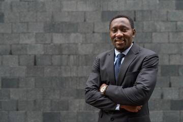 Wall Mural - Portrait of handsome African businessman in city with arms crossed smiling