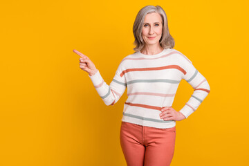 Sticker - Photo of pretty adorable lady pensioner wear striped pullover pointing finger empty space smiling isolated yellow color background