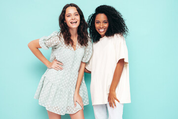 Two young beautiful smiling international hipster female in trendy summer clothes. Sexy carefree women posing near blue wall in studio. Positive models having fun. Concept of friendship