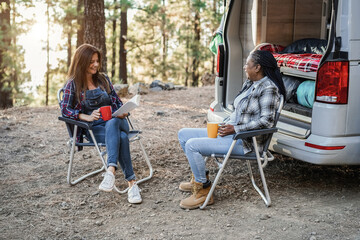 Poster - Multiracial women friends having fun camping with camper van while reading and drink coffee outdoor - Focus on african female face