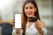 © David - Smiling Young woman holding Mockup smartphone blank white screen and credit card, payments and Online shopping, digital banking, E-commerce concept.
