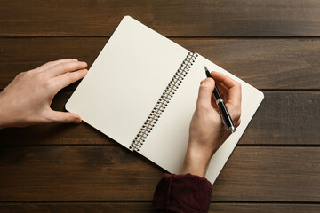 Wall Mural - Woman writing with pen in notebook at wooden table, top view