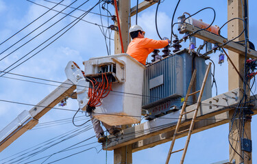 Electrician in bucket of articulated boom lift is repairing electrical transmission on power poles against blue sky background