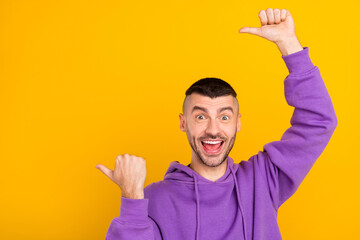 Poster - Photo portrait young man wearing purple hoody showing copyspace with thumb isolated vivid yellow color background