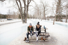 Couple Putting On Ice Skates At Picnic Table In Snowy Winter Park