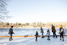 Family Ice Skating On Frozen Path Along River In Sunny Winter Park