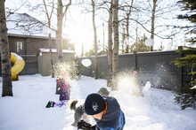 Brothers And Sister Enjoying Snowball Fight In Sunny Snowy Backyard