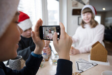 Boy Photographing Sister In Santa Hat With Gingerbread House