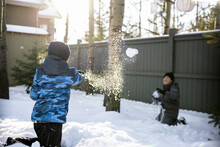 Brothers Enjoying Snowball Fight In Sunny Snowy Winter Backyard